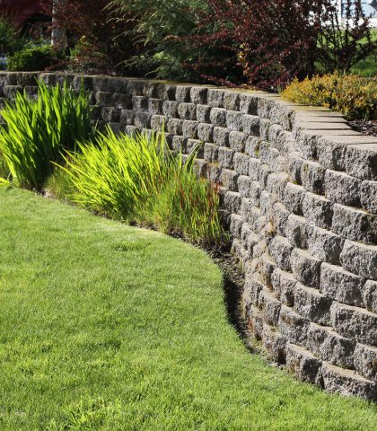 Well landscaped wall of cement cobblestone bricks with grass and ornamental plants